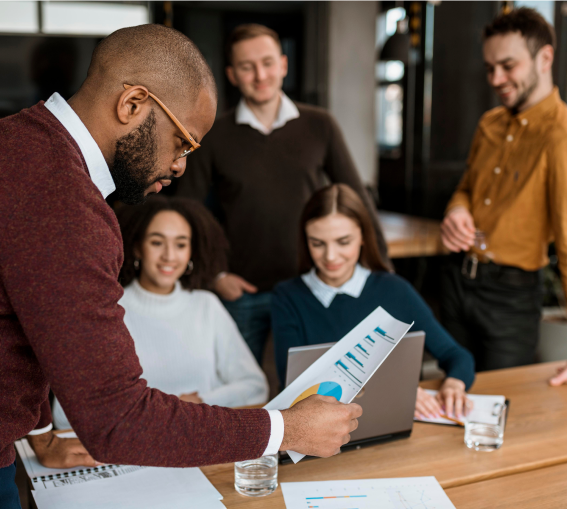 A man stands confidently before a group of attentive individuals, engaging them with his presence and words.