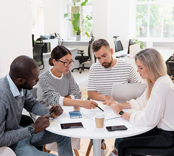 A diverse group of individuals engaged in conversation while seated around a table in a collaborative setting.