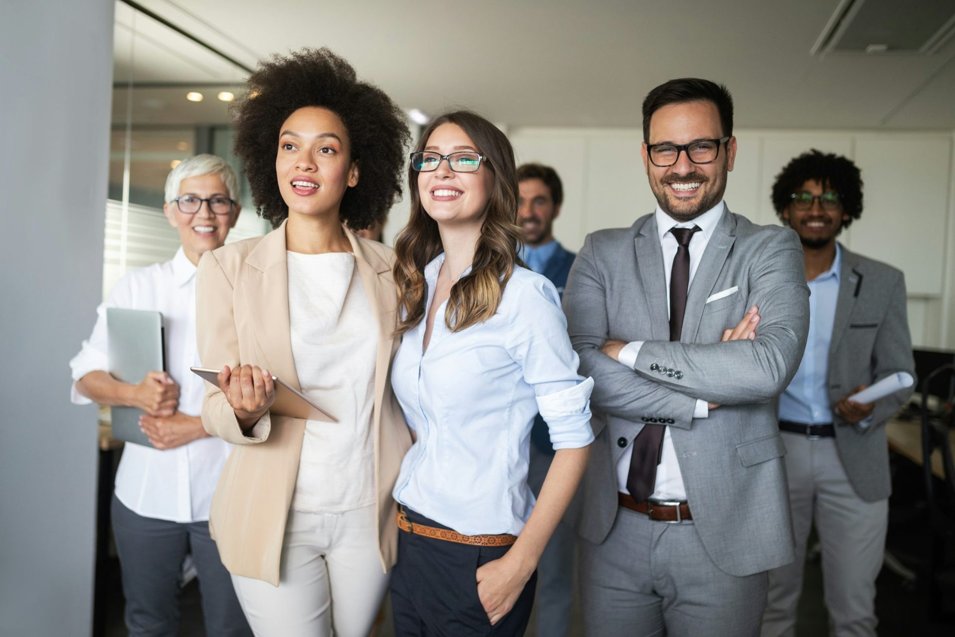 A diverse group of business professionals standing together in a modern office environment, engaged in discussion.